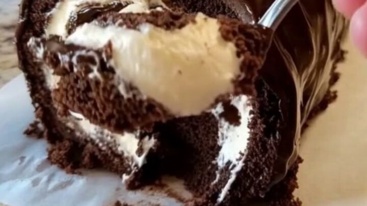 A glossy chocolate-glazed Swiss roll resting on parchment paper with a beautiful spiral visible.