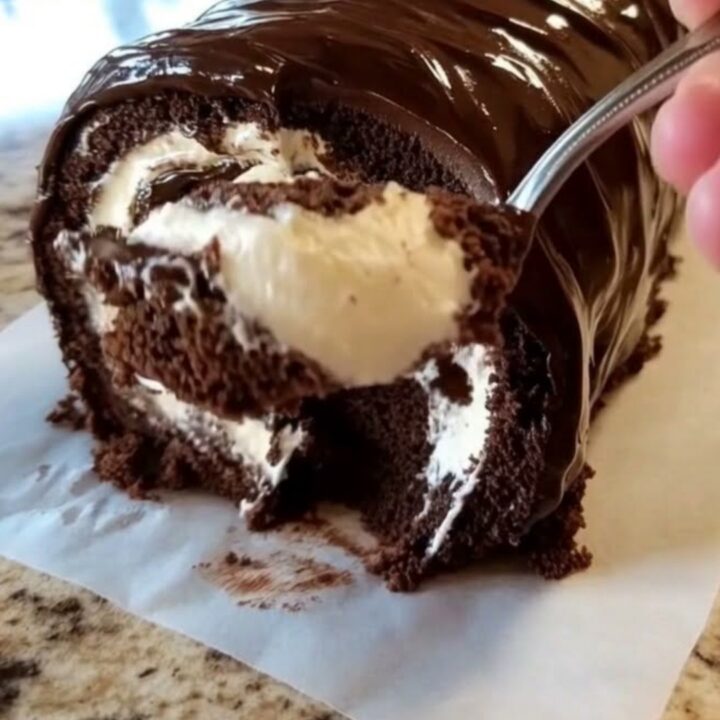 A glossy chocolate-glazed Swiss roll resting on parchment paper with a beautiful spiral visible.