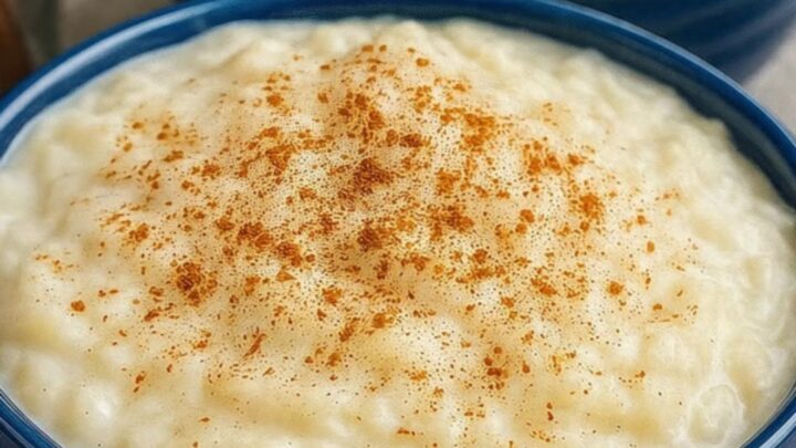 A warm bowl of rich, creamy rice pudding topped with a delicate dusting of ground cinnamon in a blue ceramic dish.