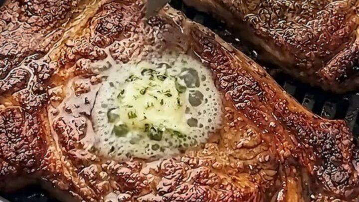 Two perfectly seared ribeye steaks topped with melting garlic herb butter on a white plate.