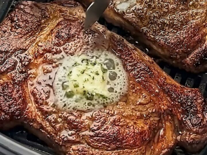 Two perfectly seared ribeye steaks topped with melting garlic herb butter on a white plate.