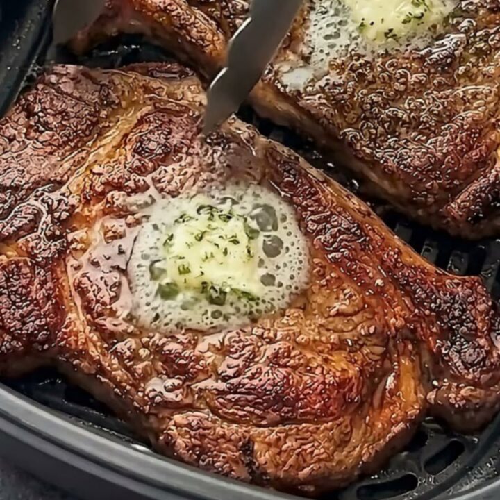 Two perfectly seared ribeye steaks topped with melting garlic herb butter on a white plate.