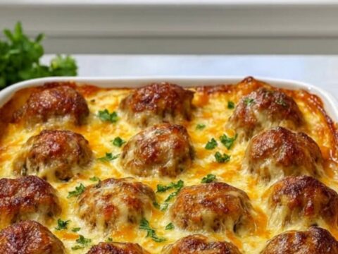 A golden, bubbling meatball casserole in a white baking dish with melted mozzarella cheese.
