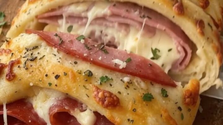 A golden-brown ham and pepperoni stromboli resting on a wooden cutting board.