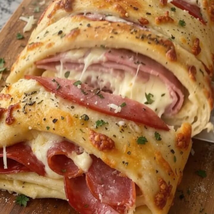 A golden-brown ham and pepperoni stromboli resting on a wooden cutting board.