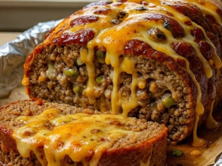 A thick slice of Philly Cheesesteak Meatloaf on a plate with melted provolone and cheddar stretching from the center.