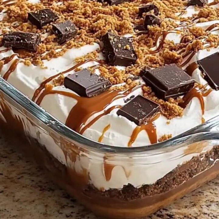 A glass dish filled with layers of chocolate pudding, caramel sauce, and whipped cream, topped with chocolate and crumbs.