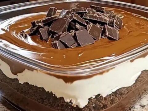 A close-up of a rich, layered chocolate dessert in a glass dish with a glossy finish and dark chocolate chunks.