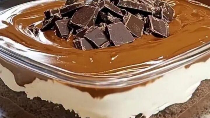 A close-up of a rich, layered chocolate dessert in a glass dish with a glossy finish and dark chocolate chunks.