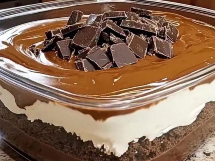 A close-up of a rich, layered chocolate dessert in a glass dish with a glossy finish and dark chocolate chunks.