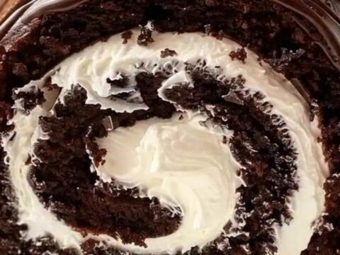 A slice of chocolate cake roll showing a perfect whipped cream swirl on a white platter.