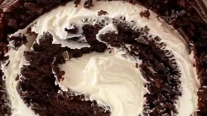 A slice of chocolate cake roll showing a perfect whipped cream swirl on a white platter.