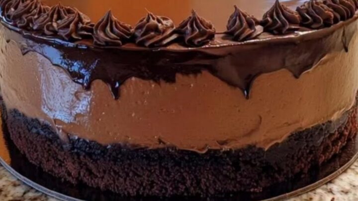A decadent chocolate mousse cake topped with glossy ganache and decorative rosettes on a cake stand.
