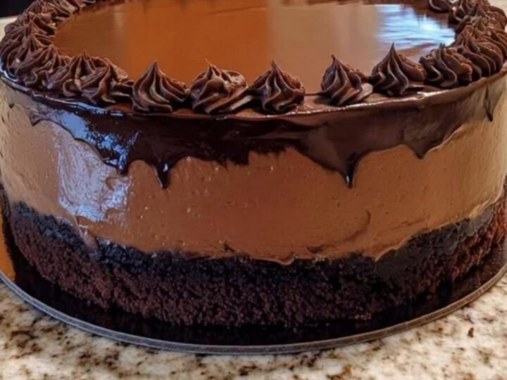 A decadent chocolate mousse cake topped with glossy ganache and decorative rosettes on a cake stand.