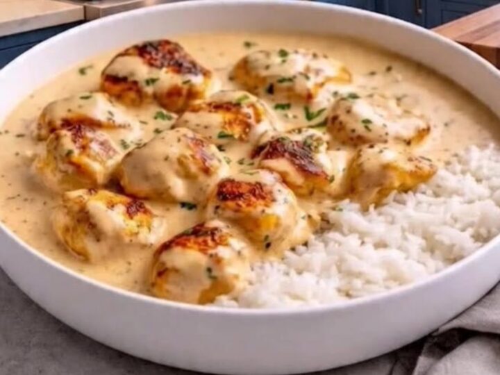 A close-up of creamy garlic chicken served with a side of fluffy white rice in a white dish.