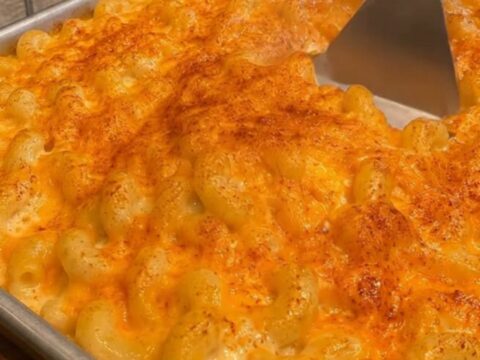 A golden, crusty baked macaroni and cheese in a metal baking pan with a spatula scooping out a portion.