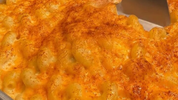 A golden, crusty baked macaroni and cheese in a metal baking pan with a spatula scooping out a portion.