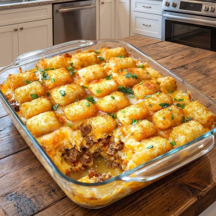 A glass baking dish filled with a golden, cheesy tater tot beef casserole sitting on a wooden kitchen counter.