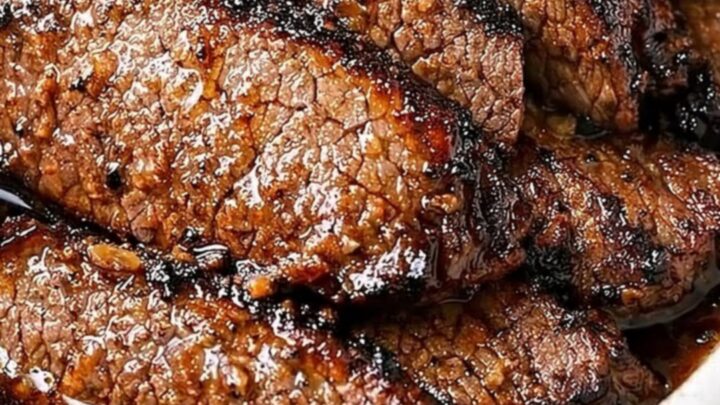 A close-up of tender, sliced garlic butter beef brisket in a white oval baking dish.