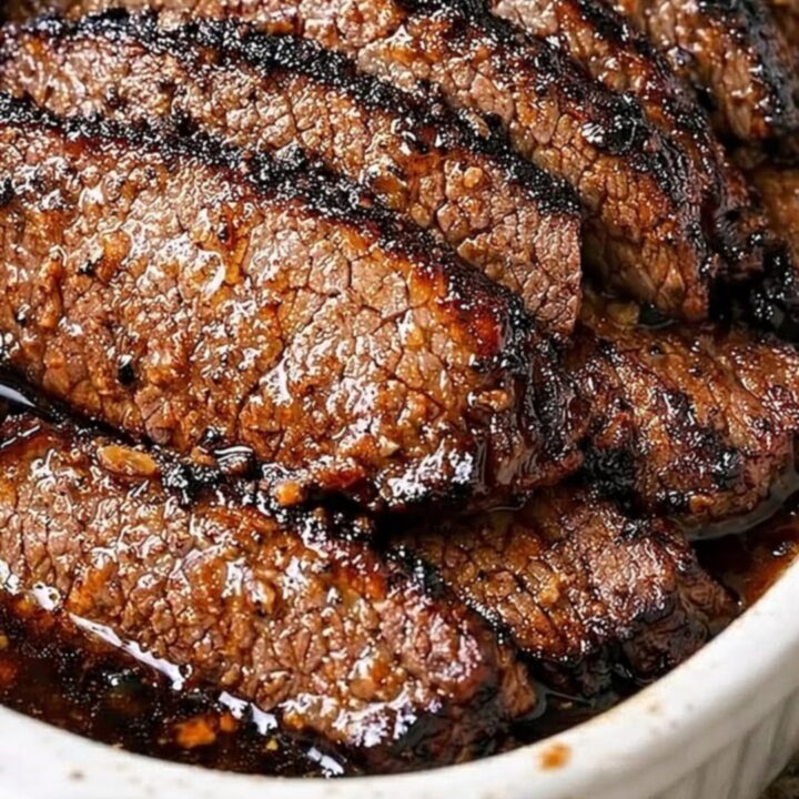 A close-up of tender, sliced garlic butter beef brisket in a white oval baking dish.