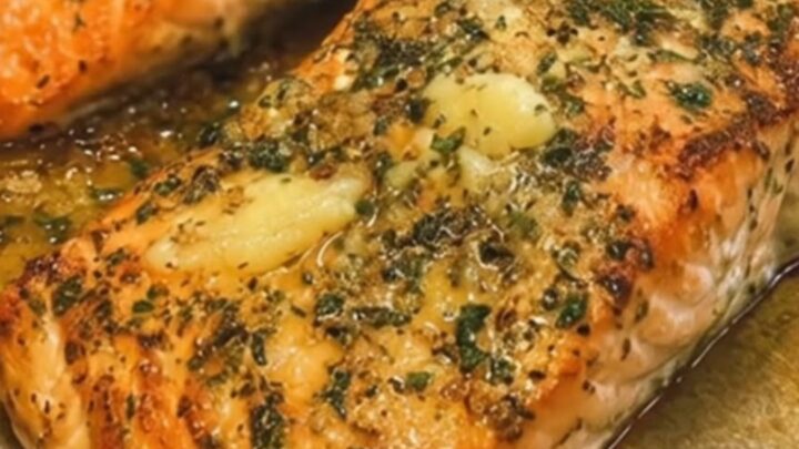 A perfectly baked salmon fillet with a golden, glistening garlic herb butter crust on a white plate.