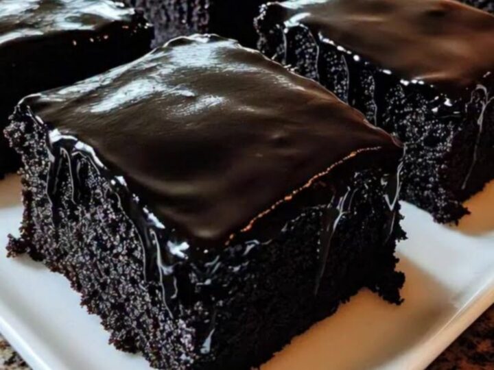 A close-up view of a rich, dark chocolate sheet cake square being lifted from a platter.