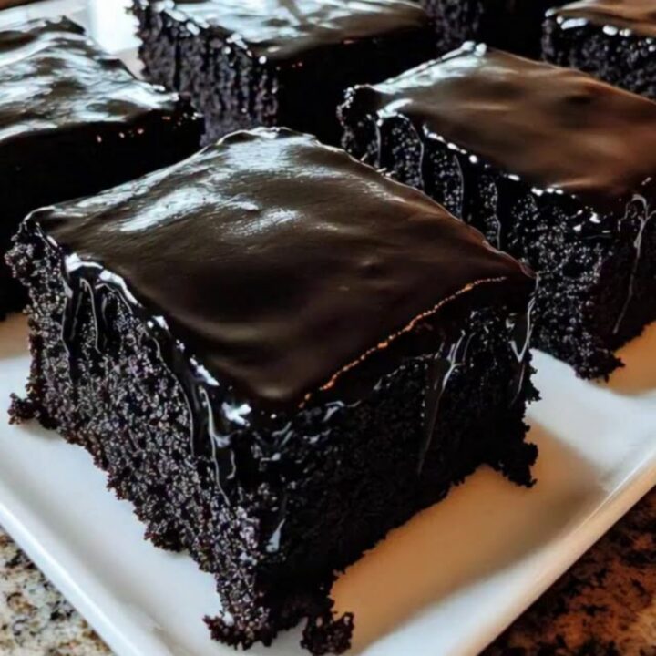 A close-up view of a rich, dark chocolate sheet cake square being lifted from a platter.