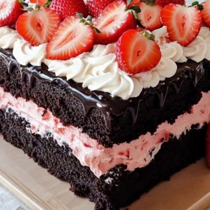 A slice of chocolate layer cake with strawberry cream filling and a chocolate ganache drip.