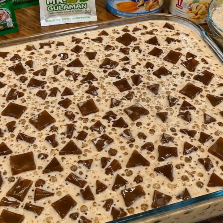 A close-up of a glass bowl filled with creamy Milo gulaman showing dark chocolate jelly cubes and sago.