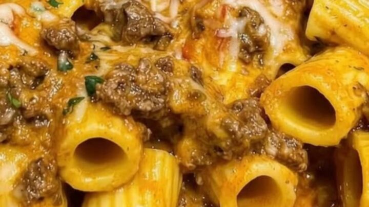 A steaming white bowl of garlic butter beef rigatoni coated in a rich orange tomato cream sauce and garnished with parsley.