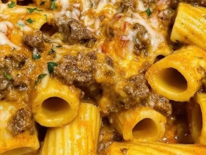 A steaming white bowl of garlic butter beef rigatoni coated in a rich orange tomato cream sauce and garnished with parsley.