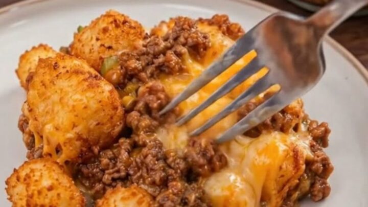 A close-up of a serving of Sloppy Joe Tater Tot Casserole in a glass dish with crispy tots on top.