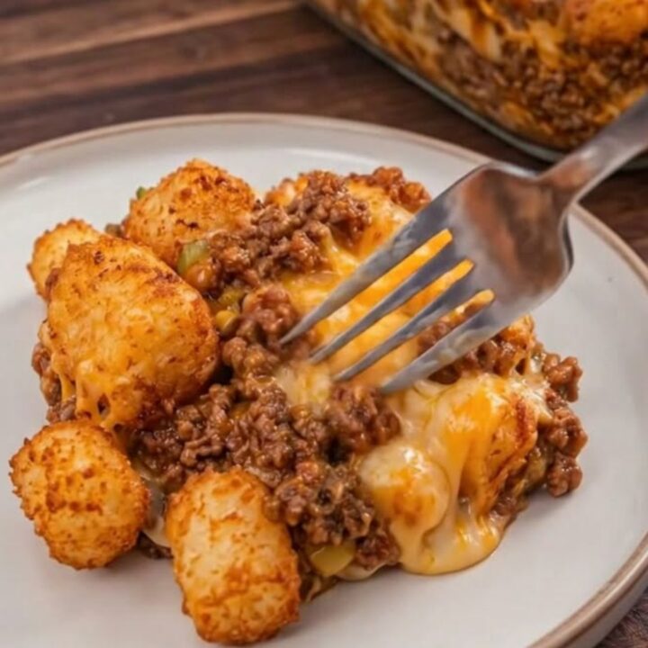 A close-up of a serving of Sloppy Joe Tater Tot Casserole in a glass dish with crispy tots on top.