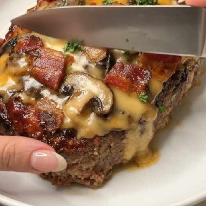 A thick slice of cheesy bacon and mushroom meatloaf on a white platter, showing steam and melted cheese.
