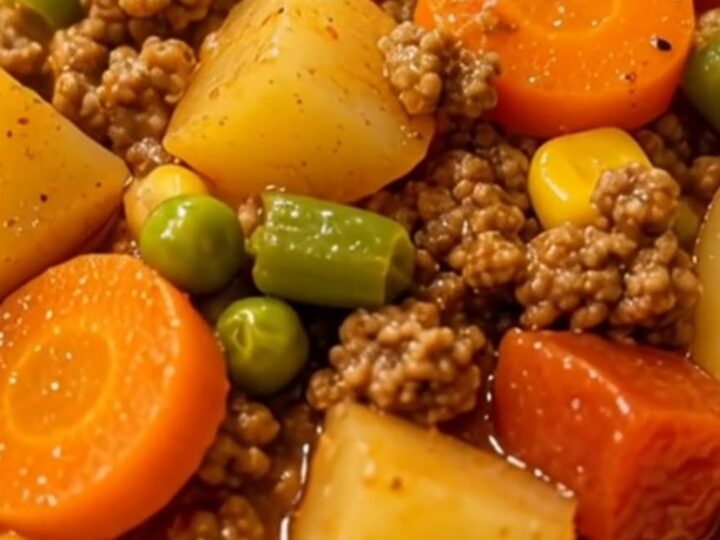 A steaming bowl of hearty vegetable beef soup filled with ground beef, potatoes, carrots, and green beans.