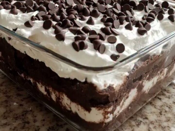 A square glass dish showing distinct layers of crushed chocolate cookies and fluffy whipped cream topped with mini chocolate