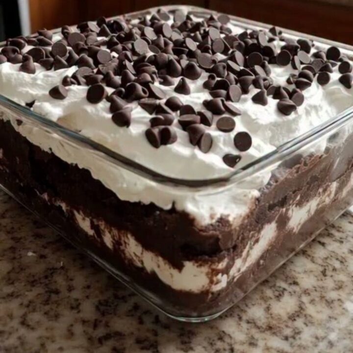 A square glass dish showing distinct layers of crushed chocolate cookies and fluffy whipped cream topped with mini chocolate