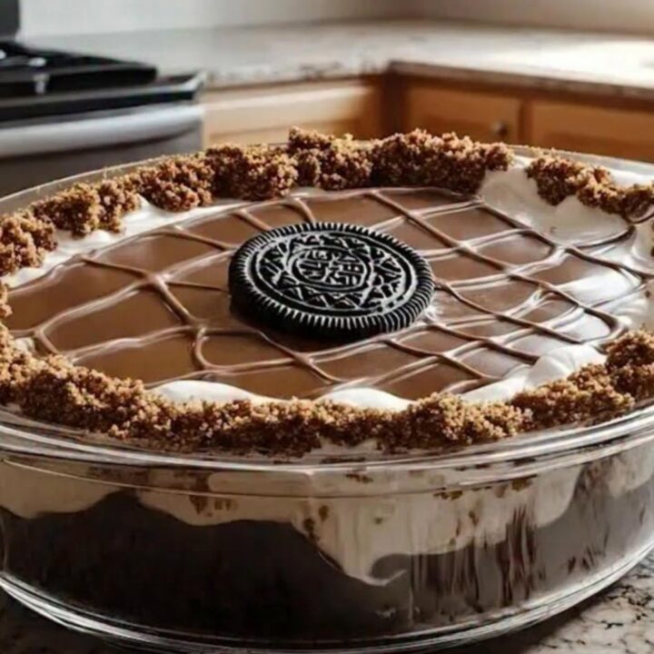 A close-up of a chilled Oreo chocolate cake in a glass dish with distinct layers of cake, cream, and ganache.