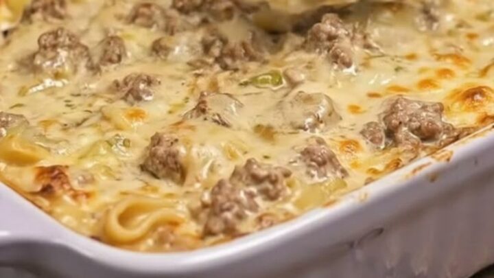 A golden, cheese-topped creamy beef stroganoff bake in a purple ceramic dish.