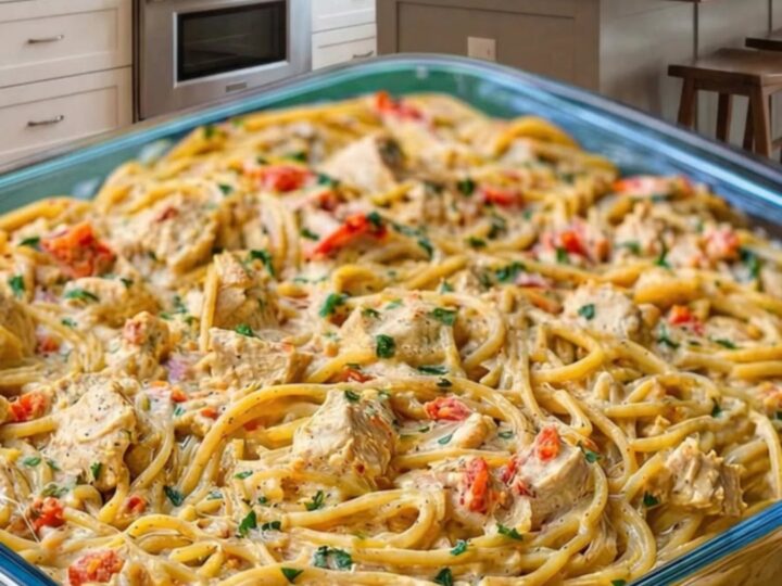 A glass baking dish filled with creamy chicken spaghetti topped with melted golden cheddar cheese.