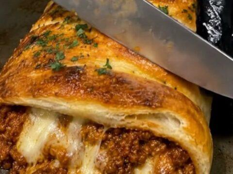 A golden, flaky baked pastry filled with seasoned ground beef and melted mozzarella on a metal baking sheet.