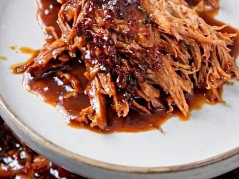A close-up of tender, shredded beef in a dark, glossy barbecue sauce inside a slow cooker.