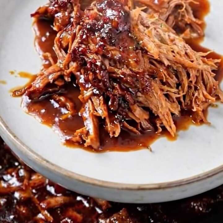 A close-up of tender, shredded beef in a dark, glossy barbecue sauce inside a slow cooker.