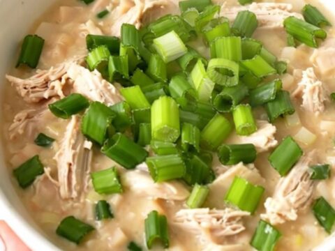 A bowl of creamy white chicken chili garnished with fresh green onions in a bright kitchen setting.