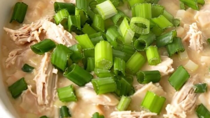 A bowl of creamy white chicken chili garnished with fresh green onions in a bright kitchen setting.