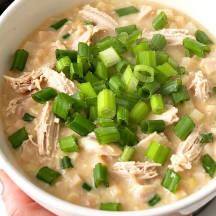A bowl of creamy white chicken chili garnished with fresh green onions in a bright kitchen setting.
