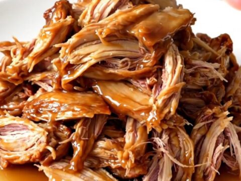 A close-up of tender, glossy apple cider pulled chicken served on a white plate.