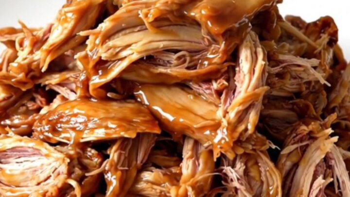 A close-up of tender, glossy apple cider pulled chicken served on a white plate.
