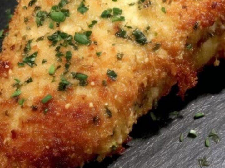 A golden-brown crispy chicken cordon bleu sliced open on a dark slate board to reveal molten cheese.