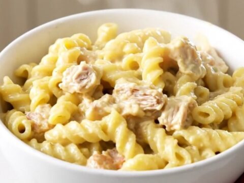 A white bowl filled with creamy chicken pot pie pasta, showing chunks of chicken and colorful vegetables in a thick sauce.